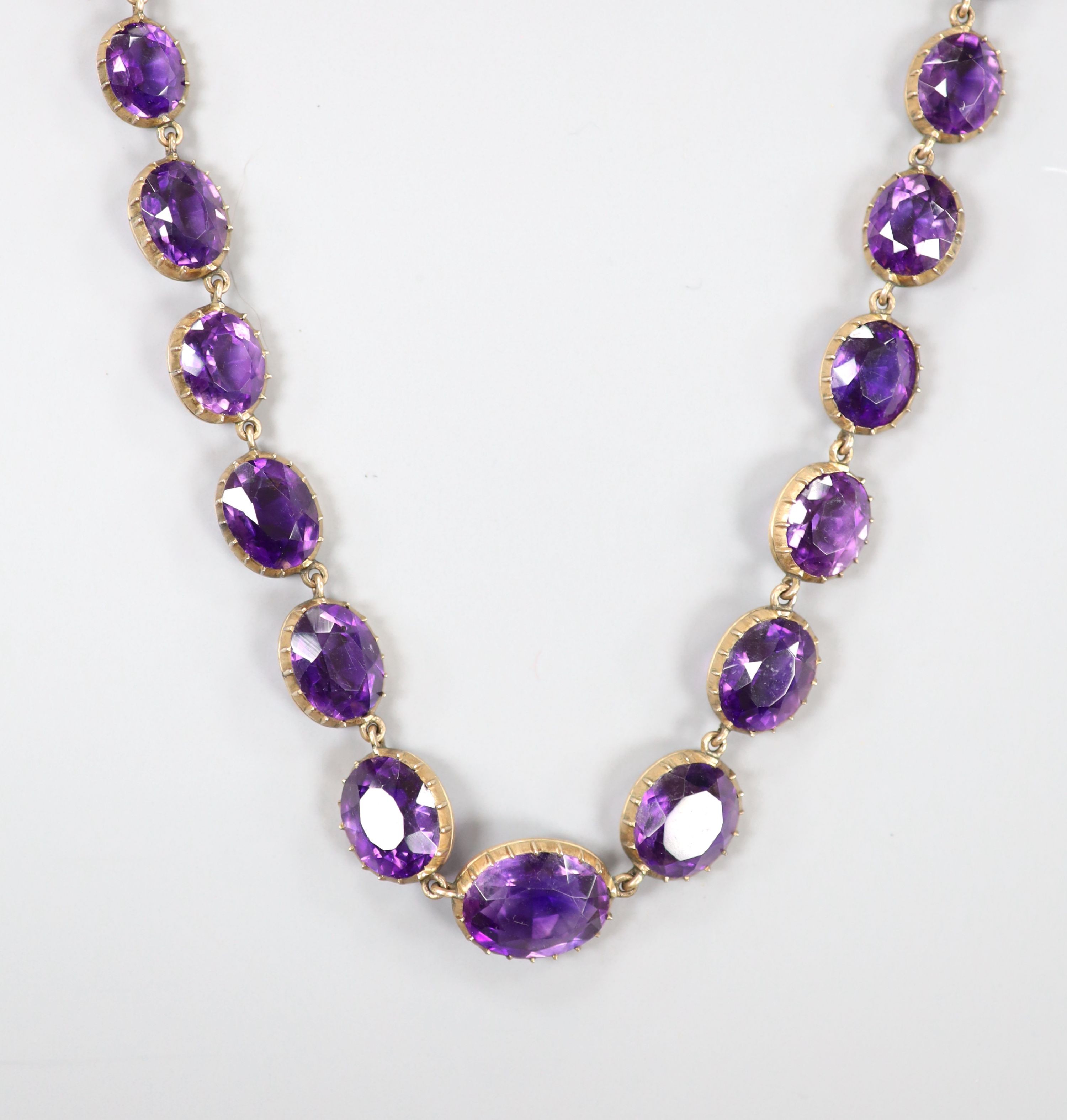 A late Victorian yellow metal and graduated oval cut amethyst set riviere necklace, 39cm, gross weight 37 grams.